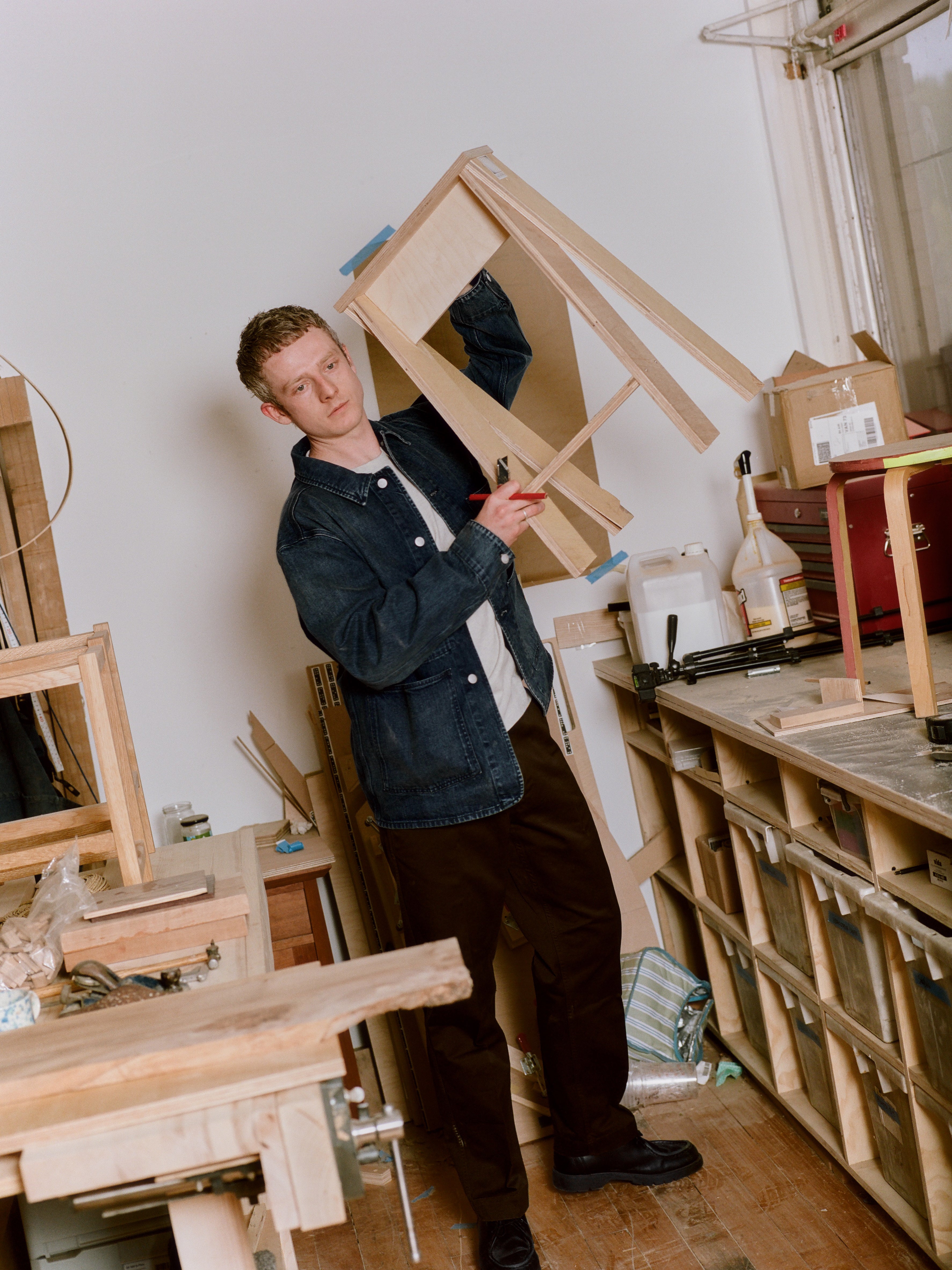 Olly Geary holding a wooden frame in a workshop setting.