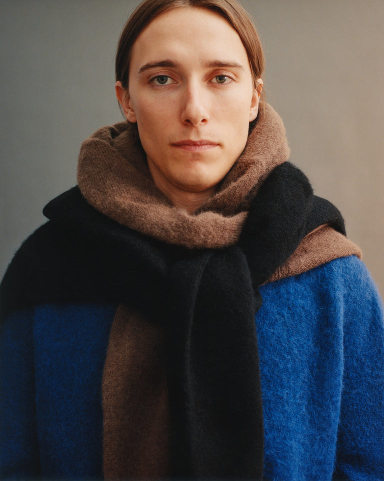 Person wearing a blue sweater and brown scarf against a neutral background